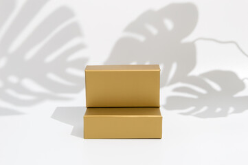Golden podium for product presentation on white background, tropical shadows of monstera leaves. Double block stand. Trendy mock up for package placement, promotion sale or cosmetic display