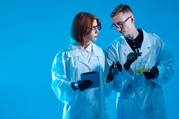 Medical researcher on blue background. Two medical researcher a test tube in hand. Young guy and a girl in uniform of doctors. Tablet computer in hands of researchers. Research in laboratory.