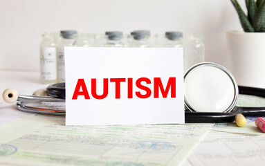 Autism word written on medical blue folder with patient files, pills and stethoscope on background.