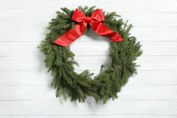 Christmas wreath made of fir branches with red bow on white wooden background