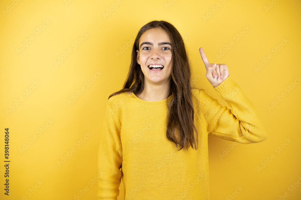 Wall mural pretty girl wearing a yellow sweater standing over isolated yellow background having an idea