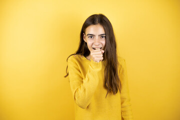 Pretty girl wearing a yellow sweater standing over isolated yellow background with her hand to her mouth coughing