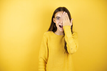 Pretty girl wearing a yellow sweater standing over isolated yellow background overing one eye with...