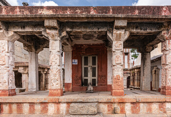 Hampi, Karnataka, India - November 4, 2013: Virupaksha Temple complex. Nandi statue in front of locked shrine under ruinous mandapam with fresco chiseled pillars.