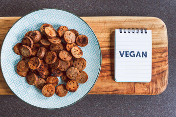 plant-based food,  vegan sausage cut into salami slices and pan fried with cracked pepper on top next to memo with Vegan written on it