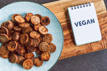 plant-based food,  vegan sausage cut into salami slices and pan fried with cracked pepper on top next to memo with Vegan written on it