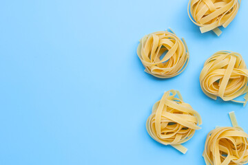 Uncooked Italian pasta tagliatelle nest on blue background. Copy space