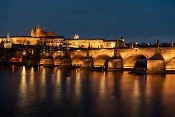 . prague castle and charles bridge and st. vita church lights from street lights are reflected on the surface of the vltava river in the center of prague at night in the czech republic