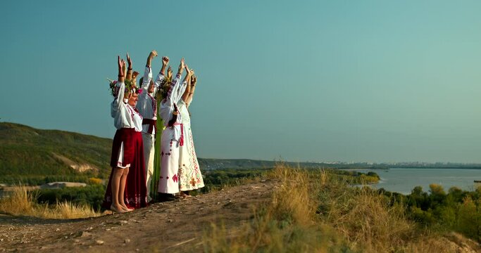 Group of women and men in folk costumes stand on the mountain and raise their hands up, folklore traditions and customs. Beautiful rural landscape. 4k, ProRes