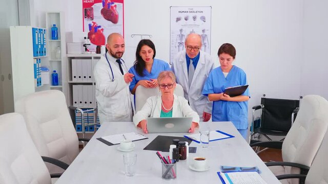 Team of doctors looking at laptop in conference room wearing medical uniform working in conference meeting room. Clinic expert therapist talking with colleagues about disease, medicine professional