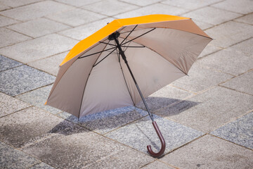 Orange umbrella on the street pavement. Parasol lies abandoned on the street single yellow parasol isolated on paved street © Holger