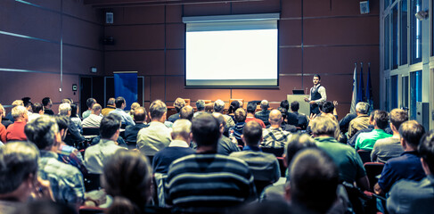 Speaker giving a talk in conference hall at business meeting event. Rear view of unrecognizable people in audience at the conference hall. Business and entrepreneurship concept.