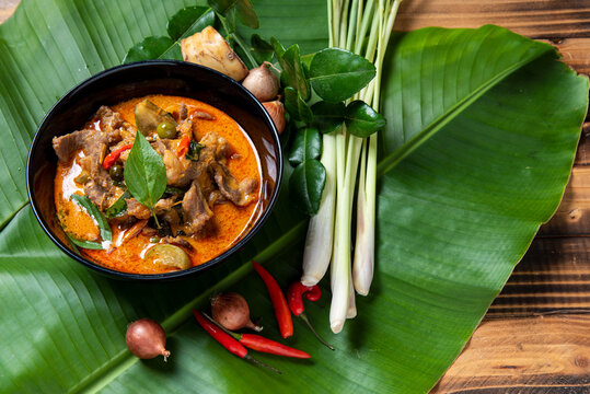 THAI BEEF RED CURRY. Thailand tradition red curry soup with beef  and coconut milk. Red Curry with ingredient in Black plate on  banana  leaf and woodden background.