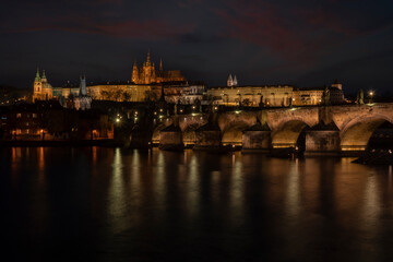 . prague castle and charles bridge and st. vita church lights from street lights are reflected on the surface of the vltava river in the center of prague at night in the czech republic