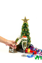A hand holding champagne glass. Bottle of champagne and christmas tree with garlands on the background. Template for wallpaper, postcard, poster design, banner. Studio shot, high quality photo