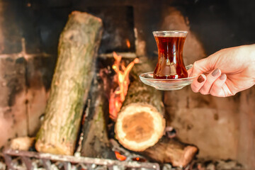 Closeup of cup with famous traditional Turkish tea in front cozy and worm fireplace, in country house. Winter or autumn (fall) vacation in Turkey. 