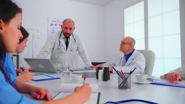 Medical staff talking with teamworker practitioner wearing white coat in hospital meeting room. Clinic therapist with colleagues talking about disease, expert,specialist, communication.