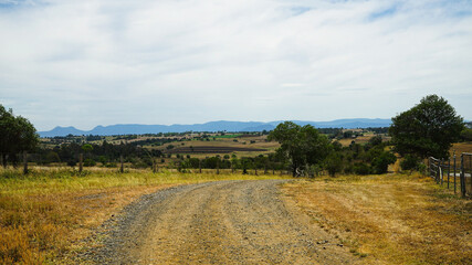 Fototapeta premium Panoramic rural landscape with gravel road in the foreground and mountains in the distance. Scenic Rim, Queensland, Australia.