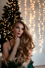 Young beautiful blonde woman in a green dress on Christmas, a woman in a room on holiday background Christmas tree, Happy New Year. Christmas woman