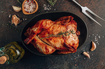 Homemade chicken roasted with thyme, garlic on a black board on a dark table.