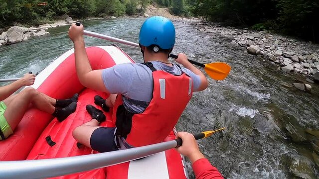Rafting. Men sit in red inflatable boat, paddle and float mountain river
