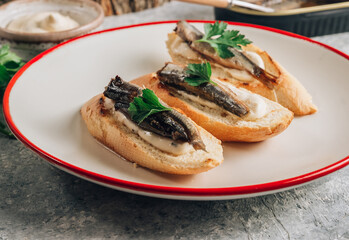 Homemade sandwich with sprats, sauce and parsley on white plate over gray background.