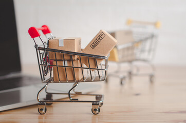 Brown paper boxs in shopping cart with laptop on wood table in office background.Easy shopping with finger tips for consumers.Online shopping and delivery service concept.