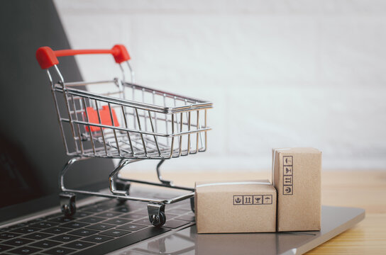 Brown paper boxs and cart with laptop on wood table in office background.Easy shopping with finger tips for consumers.Online shopping and delivery service concept.