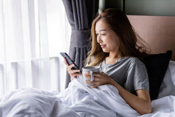 Beautiful long hair women play smartphone on the bed while hold a glass in her left hand.