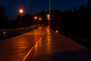 Dark pedestrian bridge lit up by street lights over rowing canal in Plovdiv, Bulgaria