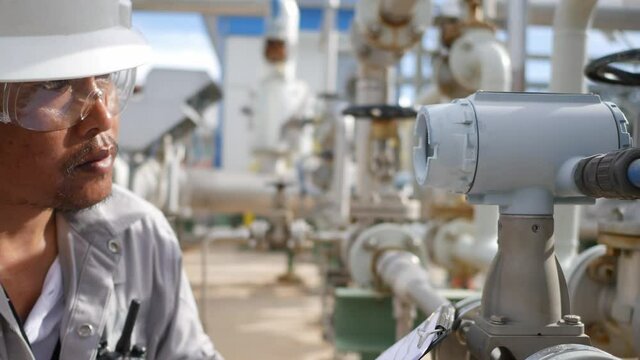 An employee holding a clipboard examining something in an industrial plant and recording the results on a paper sheet.