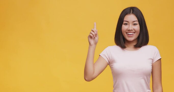 Young asian lady having idea, pointing finger up , standing over orange studio background with empty space