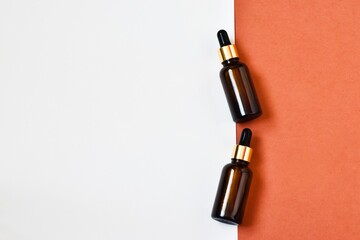 Fototapeta premium Two dropper oil bottles. Serum oil in glass bottles with a dropper on a pink-white background. Natural organic cosmetic, eco lotion, essence, serum. Copy space, flat lay. Advertising.