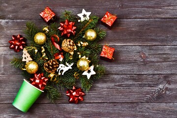 Christmas creative composition. Paper cup and fir branches with Christmas toys on a wooden background. Christmas and New year concept. Copy space, flat lay.
