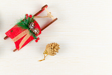 red sleigh of santa claus with fir-tree cones and green spruce branches against a background of white wood with gold veins