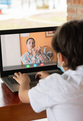 young latin boy sitting in front of a laptop computer receiving classes online by video call