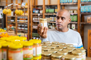 Latin american man reading jar contents on label while shopping in food department of supermarket