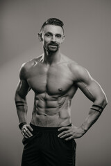Fototapeta na wymiar Black and white photo of a muscular man with a beard who is posing. The athletic guy is demonstrating his sporty physique.