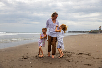 Father with daughters walking barefoot along the beach holding hands. Family relation. Vacation in Asia. Summer holidays. Happy family spending time together. Copy space. Bali island.