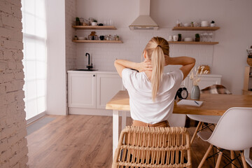 Blonde female sitting at the table and massaging her neck. Osteoporosis and spone problems. Horizontal view