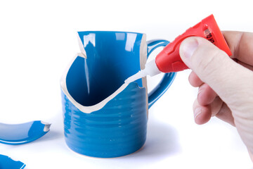 Human hand laying down a line of glue on a shattered mug