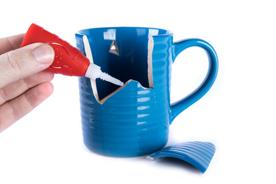 Left hand applying glue to a broken ceramc coffee cup
