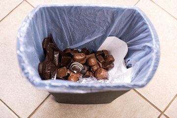 Tempting unhealthy chocolates disposed of in a garbage can at the beginning of a diet