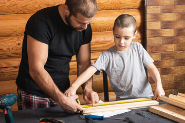 Father and son together make a wooden birdhouse in the workshop. Cheerful father with little boy...
