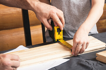 close up of the father and son together make a wooden birdhouse in the workshop. Cheerful father with little boy measure with tape measure wooden planks on table in workshop