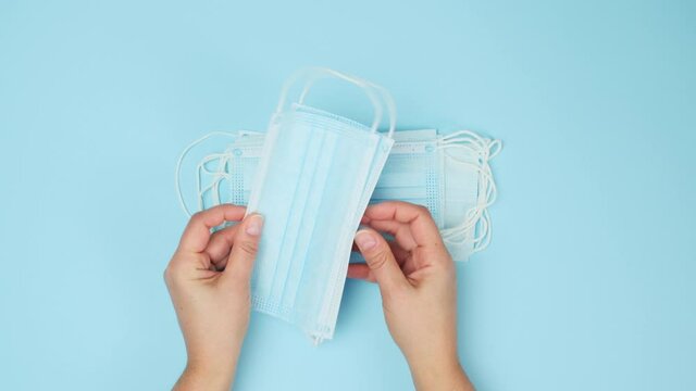 two female hands hold a stack of disposable face masks on a blue table, protection against viral diseases during a pandemic, top view