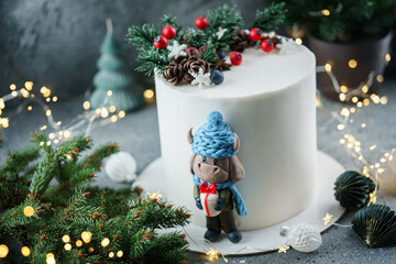 Christmas cake decorated with sweet figures berries, pine cones and the symbol of the year bull on bright background with garland, fir branches, bokeh. Winter baking at Xmas or New Year holiday