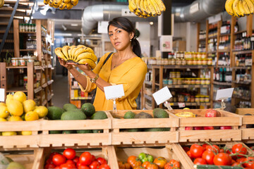 Woman shopper chooses ripe banana at grocery supermarket