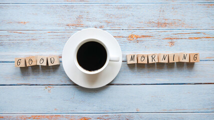 Top view of a cup of coffee and a wooden cubes written with Good Morning on a wooden background.