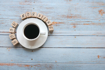 Top view of a cup of coffee and a wooden cubes written with Good Morning on a wooden background with copy space.